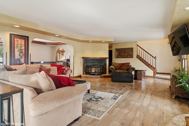 living area with arched walkways, baseboards, stairway, wood-type flooring, and a wood stove