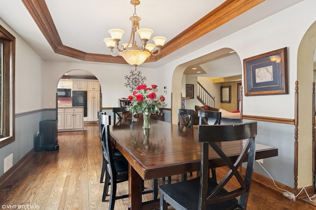 dining area with arched walkways, a tray ceiling, a notable chandelier, ornamental molding, and wood finished floors