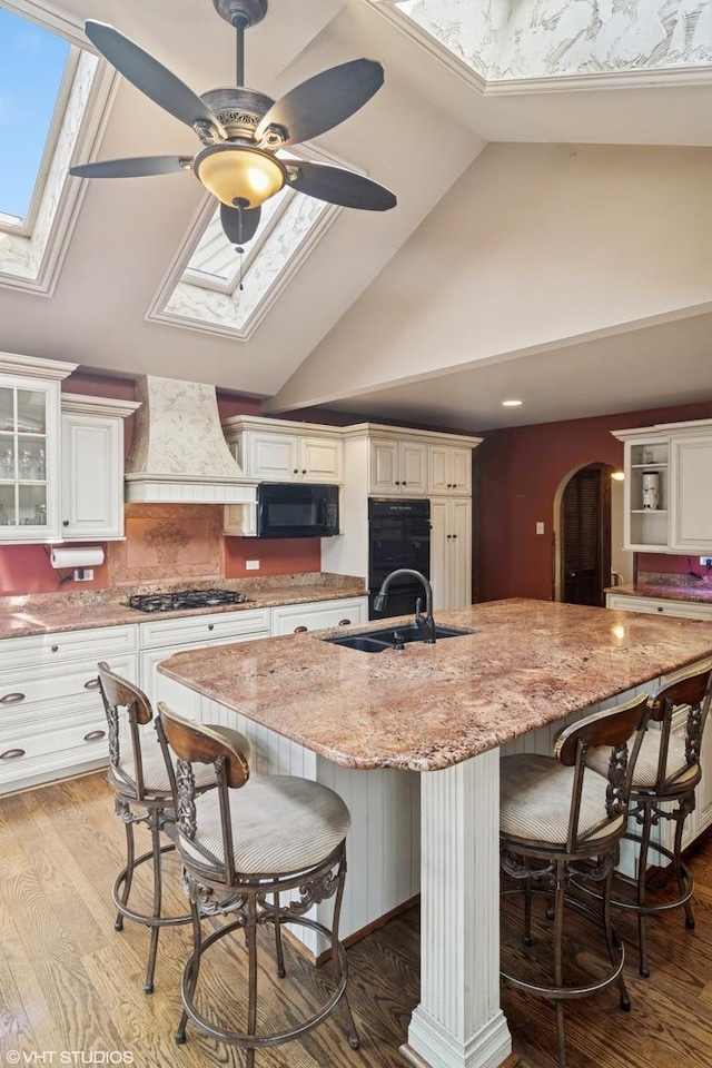 kitchen featuring a skylight, arched walkways, custom range hood, black appliances, and a sink