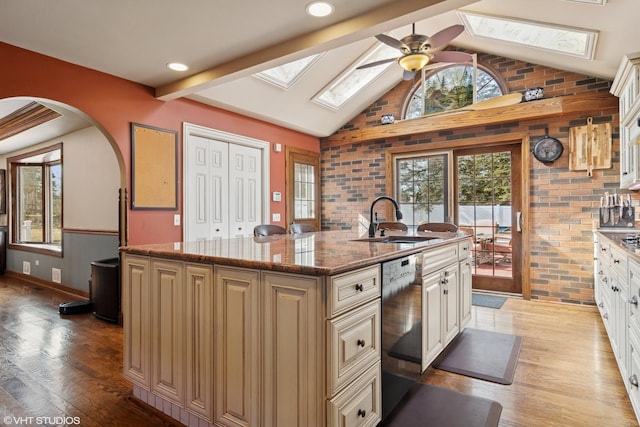 kitchen featuring light wood finished floors, lofted ceiling with skylight, a sink, an island with sink, and dishwasher