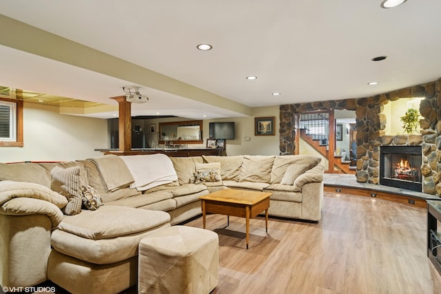 living room with recessed lighting, a stone fireplace, light wood finished floors, and stairs