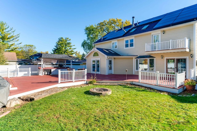 back of house with a fire pit, a lawn, fence, a wooden deck, and roof mounted solar panels