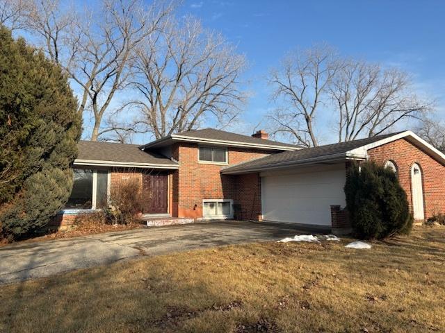 split level home featuring a garage, a chimney, aphalt driveway, a front lawn, and brick siding