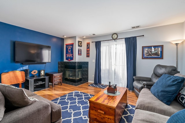 living area with baseboards, visible vents, a tiled fireplace, and wood finished floors