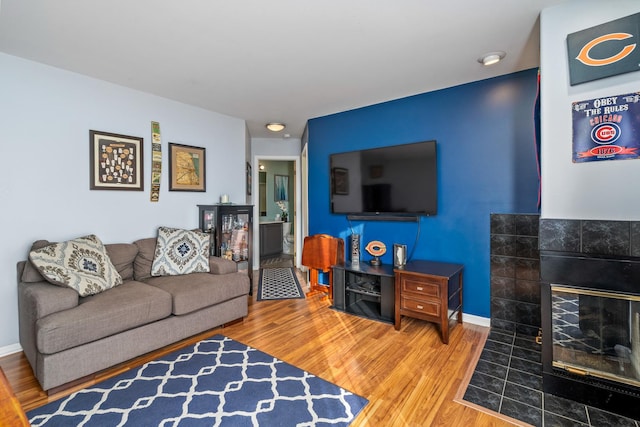 living room with a tiled fireplace, baseboards, and wood finished floors