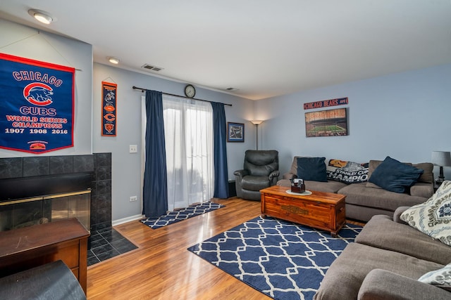 living area featuring baseboards, a fireplace, visible vents, and wood finished floors