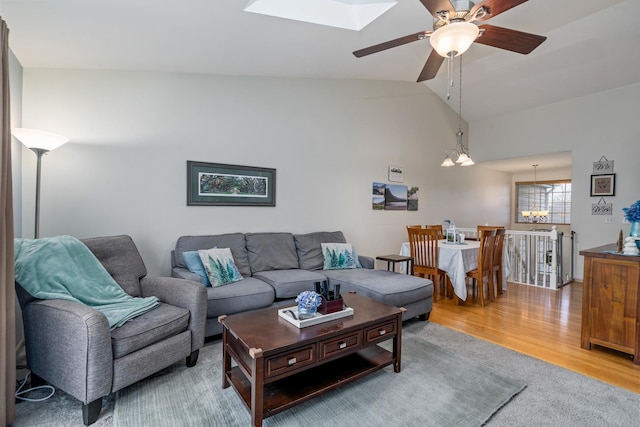 living room featuring ceiling fan with notable chandelier, vaulted ceiling with skylight, and light wood-style flooring