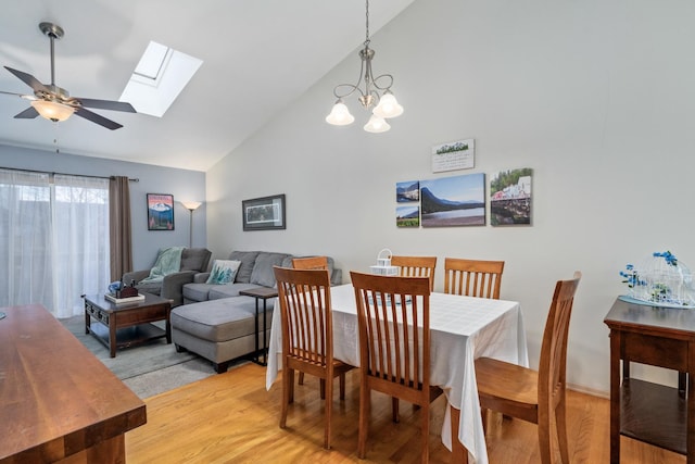 dining room featuring light wood finished floors, a skylight, high vaulted ceiling, and a ceiling fan