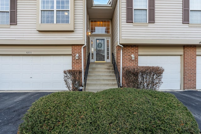 entrance to property with driveway, an attached garage, and brick siding