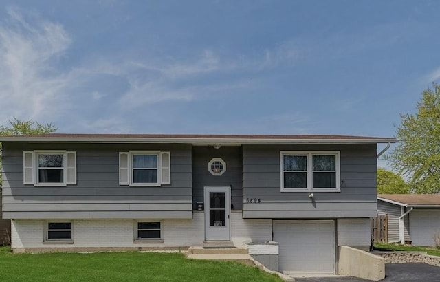 bi-level home featuring a garage, entry steps, brick siding, and a front lawn