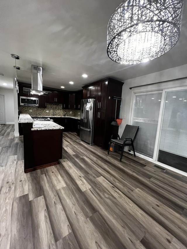 kitchen featuring light stone counters, island range hood, a kitchen island, dark brown cabinets, and appliances with stainless steel finishes