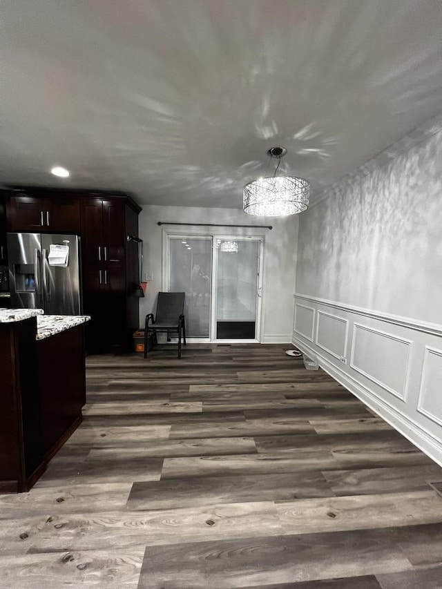 unfurnished dining area with wainscoting, dark wood finished floors, an inviting chandelier, and a decorative wall