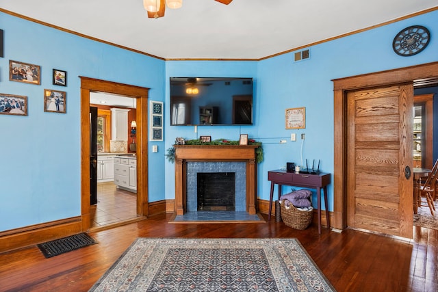 living room with a tile fireplace, wood-type flooring, visible vents, and crown molding