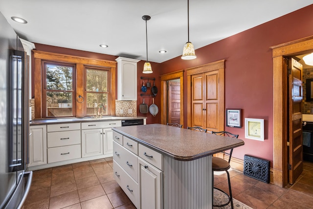 kitchen featuring high quality fridge, a breakfast bar area, a center island, dark tile patterned floors, and white cabinetry