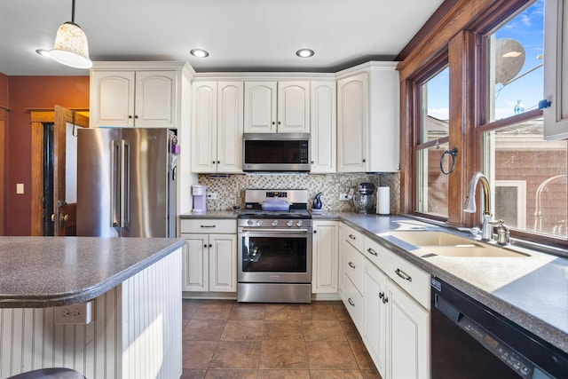 kitchen featuring white cabinets, hanging light fixtures, a sink, stainless steel appliances, and backsplash