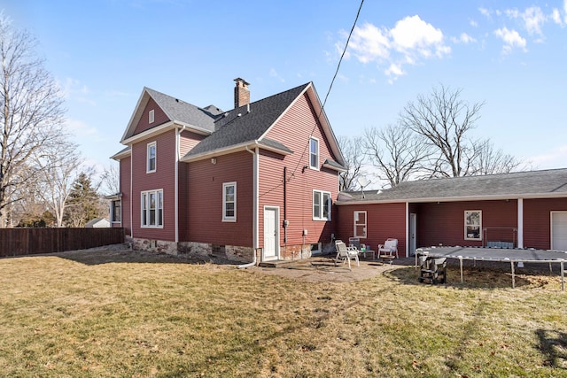 back of house featuring a lawn, a patio, a chimney, a trampoline, and fence