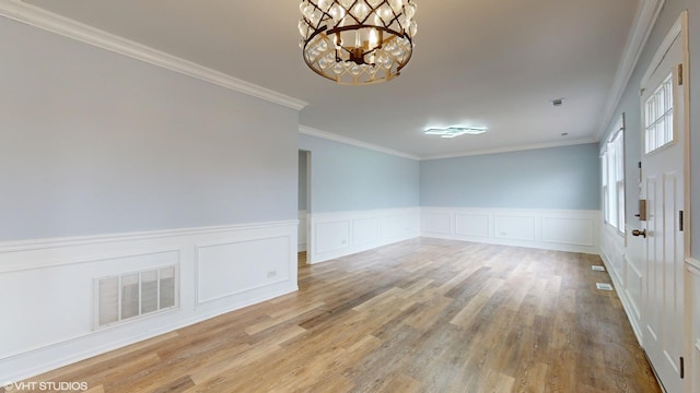 unfurnished room with visible vents, crown molding, an inviting chandelier, and wood finished floors