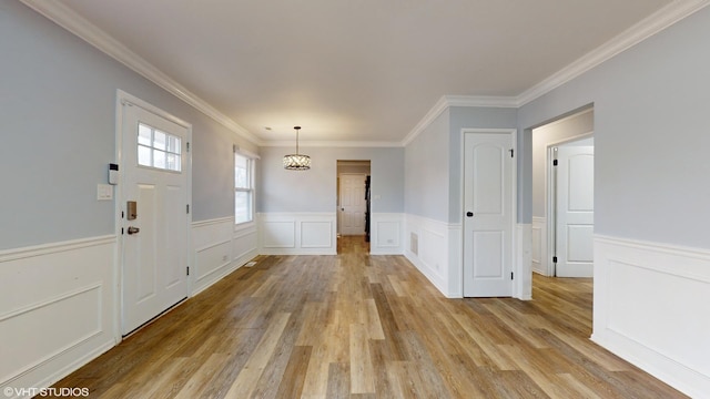 foyer featuring ornamental molding, a wainscoted wall, and light wood finished floors