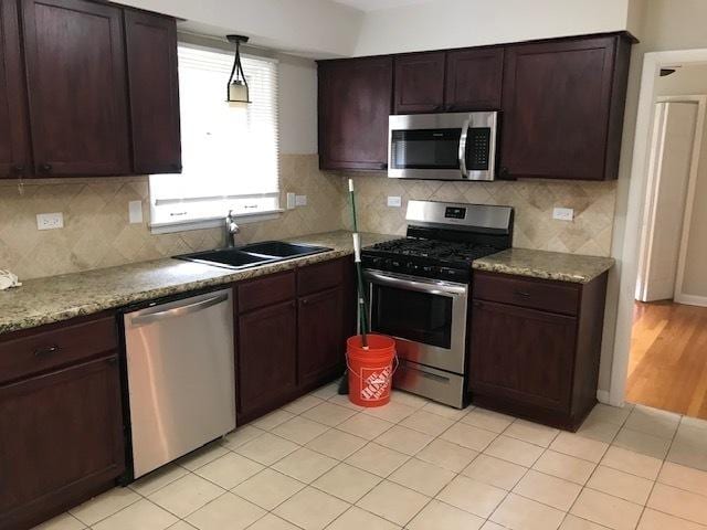 kitchen with dark brown cabinetry, decorative backsplash, appliances with stainless steel finishes, pendant lighting, and a sink