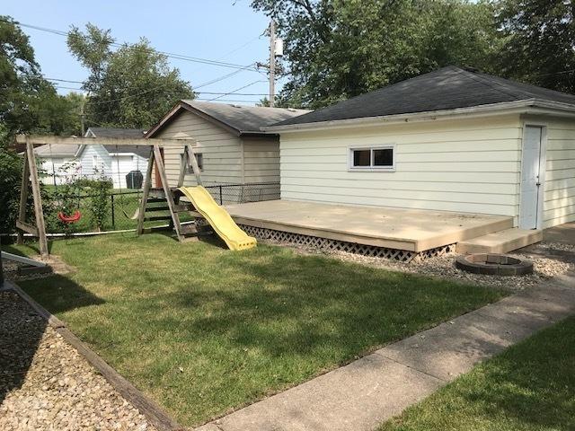 rear view of property featuring a playground, a yard, a deck, and fence