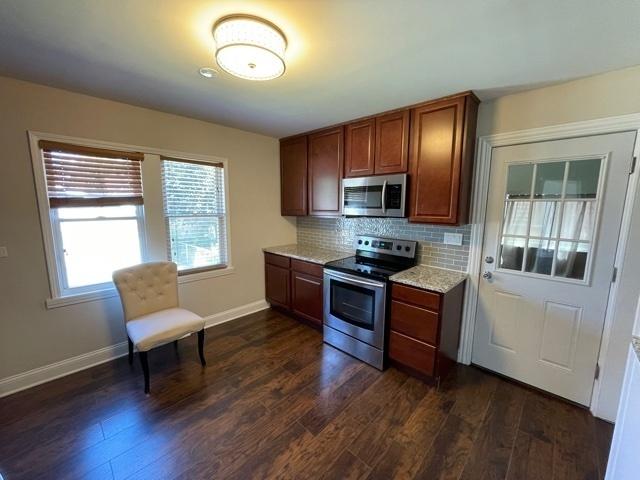 kitchen with baseboards, decorative backsplash, light stone counters, appliances with stainless steel finishes, and dark wood-type flooring