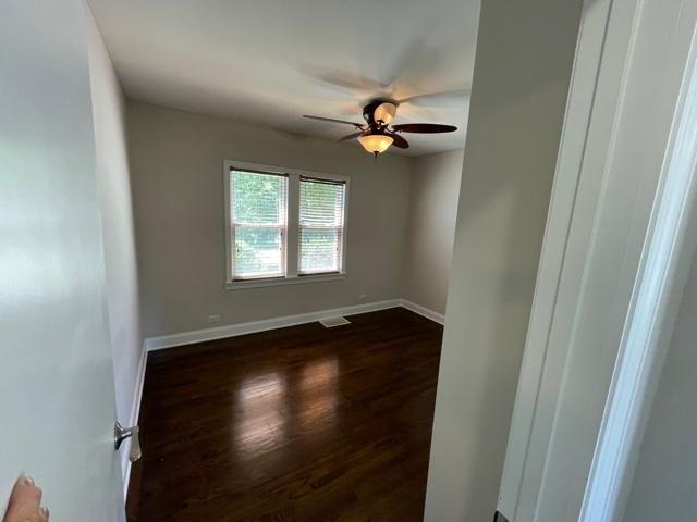 spare room featuring a ceiling fan, visible vents, dark wood finished floors, and baseboards