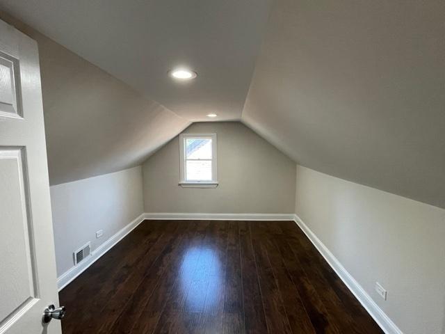 additional living space featuring hardwood / wood-style flooring, baseboards, visible vents, and vaulted ceiling