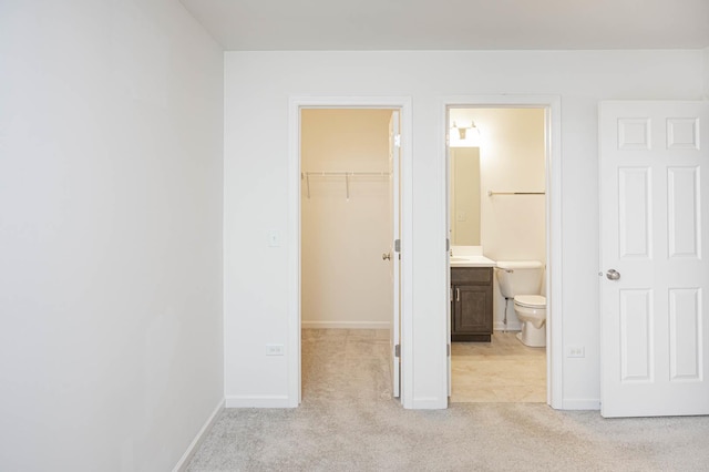 unfurnished bedroom with light carpet, baseboards, a walk in closet, and a closet