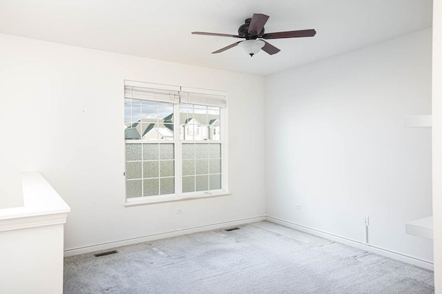 carpeted spare room with visible vents, baseboards, and a ceiling fan