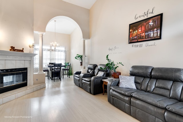 living area with light wood-type flooring, an inviting chandelier, decorative columns, and a fireplace