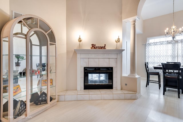 living room with ornate columns, a notable chandelier, a tiled fireplace, and wood finished floors