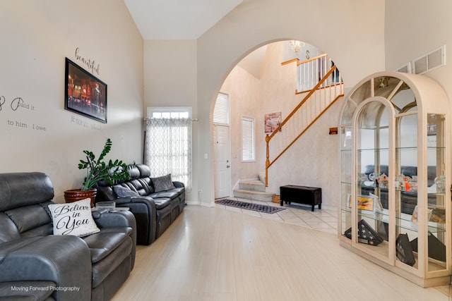 living room with light wood-style floors, visible vents, stairway, and a high ceiling