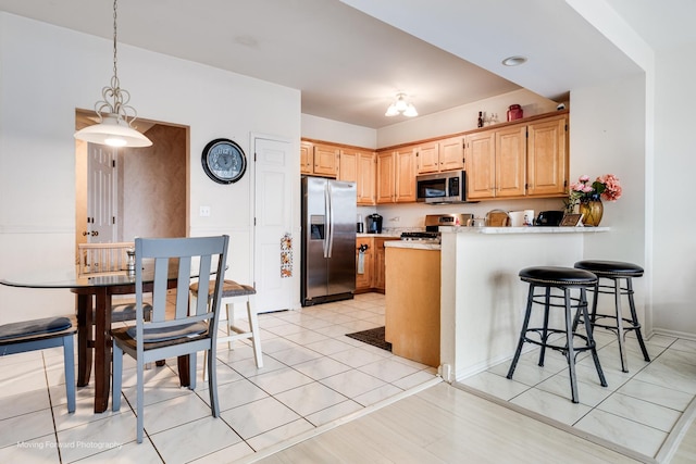 kitchen featuring a peninsula, light countertops, appliances with stainless steel finishes, hanging light fixtures, and light brown cabinetry