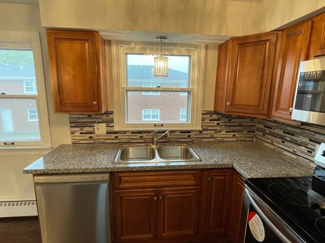 kitchen with a baseboard heating unit, appliances with stainless steel finishes, a sink, and brown cabinets