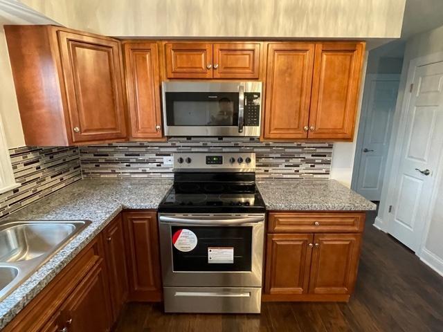 kitchen with dark wood finished floors, tasteful backsplash, appliances with stainless steel finishes, brown cabinetry, and a sink