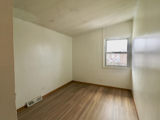 unfurnished room featuring lofted ceiling, baseboards, visible vents, and wood finished floors