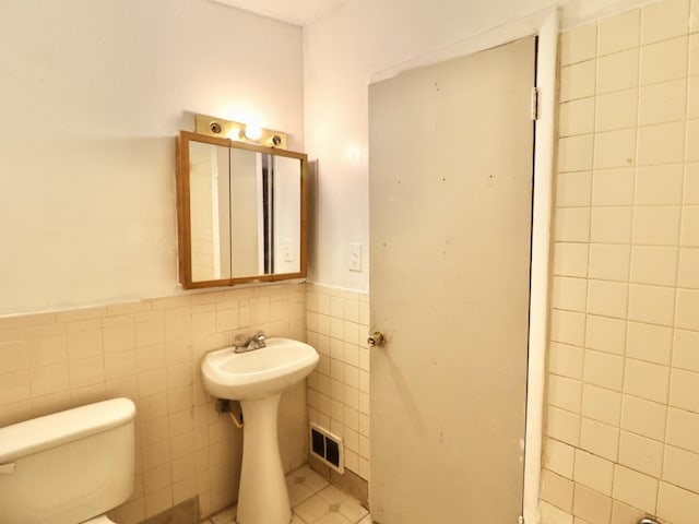 bathroom featuring a wainscoted wall, toilet, visible vents, and tile walls