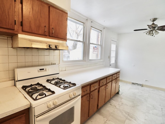 kitchen featuring white range with gas cooktop, visible vents, decorative backsplash, light countertops, and under cabinet range hood