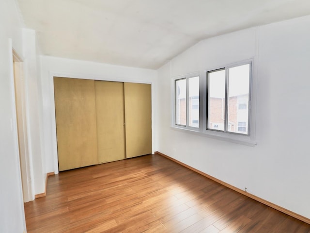 unfurnished bedroom with light wood-style floors, lofted ceiling, a closet, and baseboards