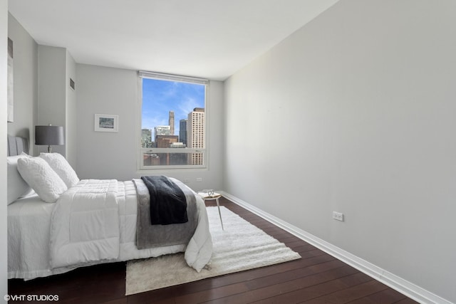 bedroom with baseboards, dark wood-type flooring, and a city view