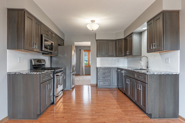 kitchen with appliances with stainless steel finishes, a sink, light stone counters, and light wood-style floors