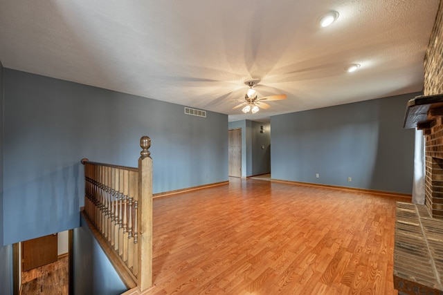 unfurnished living room with a textured ceiling, a fireplace, wood finished floors, visible vents, and baseboards