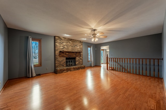 unfurnished living room featuring a ceiling fan, light wood-type flooring, visible vents, and a brick fireplace