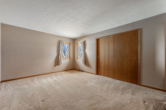 unfurnished bedroom with baseboards, visible vents, light colored carpet, a textured ceiling, and a closet