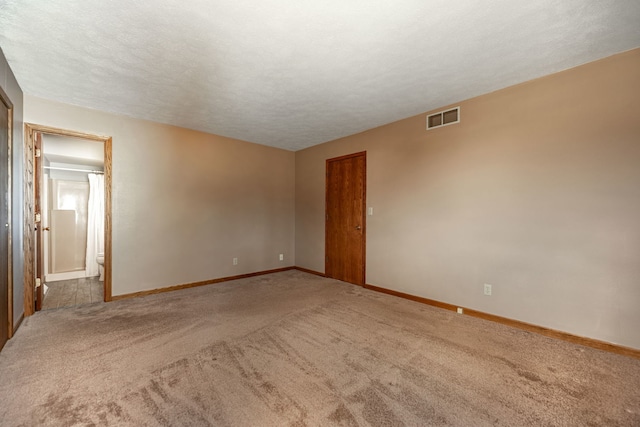 unfurnished room with a textured ceiling, carpet flooring, visible vents, and baseboards