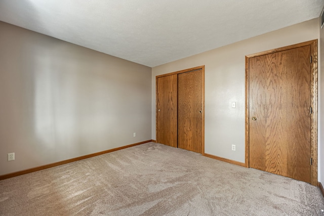 unfurnished bedroom featuring a closet, light carpet, a textured ceiling, and baseboards