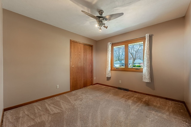 carpeted empty room featuring a textured ceiling, a ceiling fan, visible vents, and baseboards