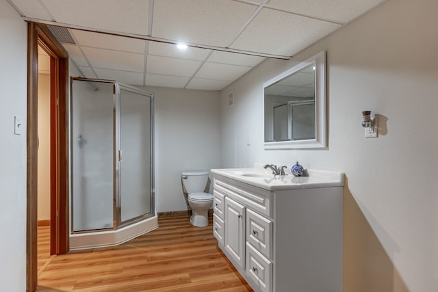 bathroom with toilet, a shower stall, vanity, wood finished floors, and a drop ceiling