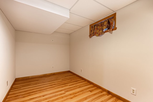 spare room featuring light wood finished floors, a paneled ceiling, and baseboards