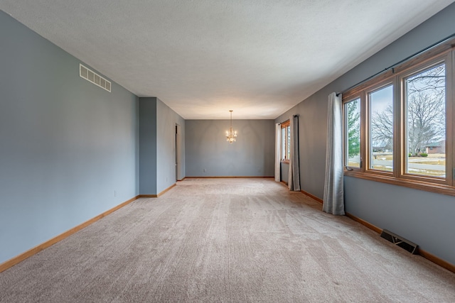 spare room with baseboards, visible vents, a chandelier, and a textured ceiling